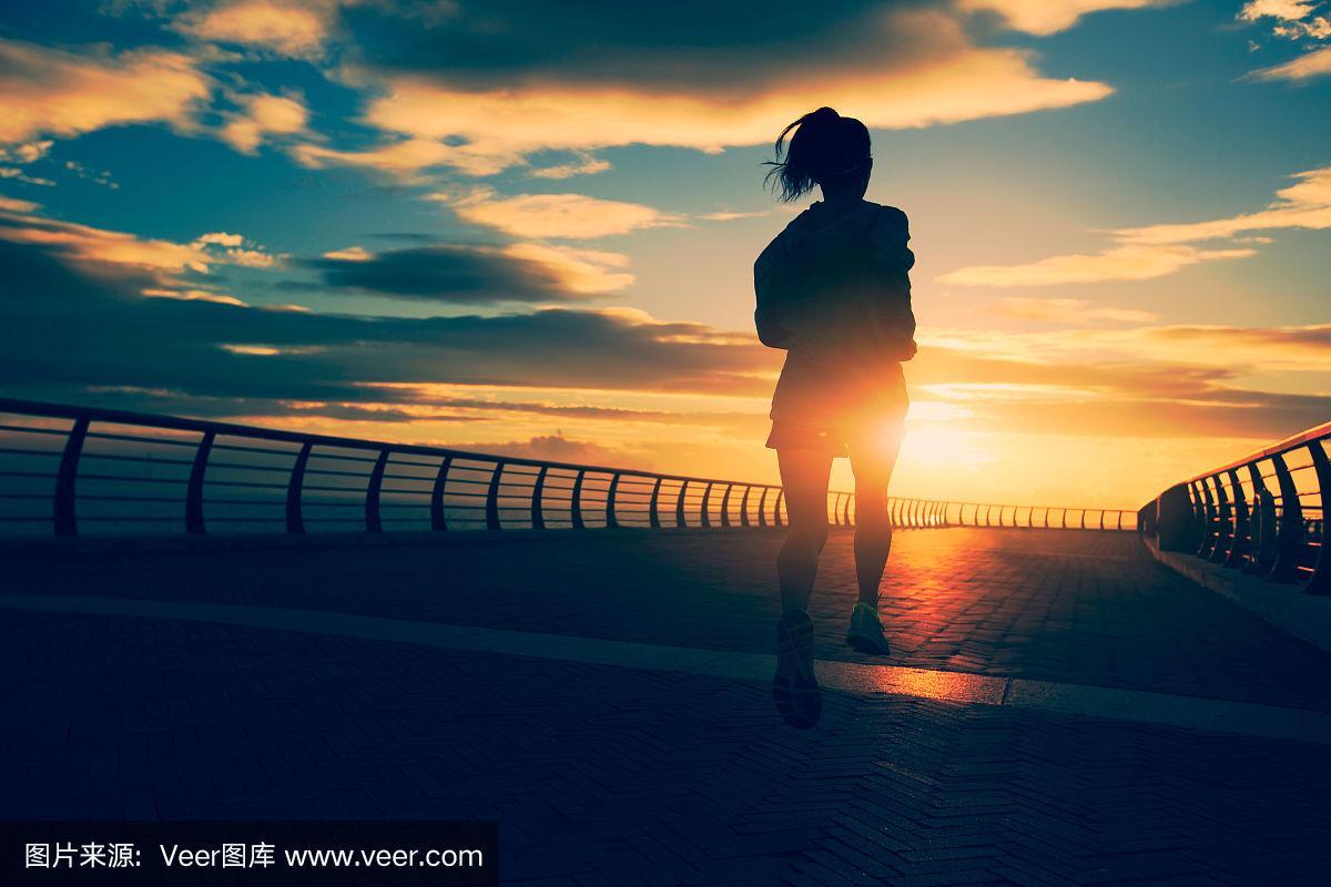 年轻的健身女性跑步在日出的海边