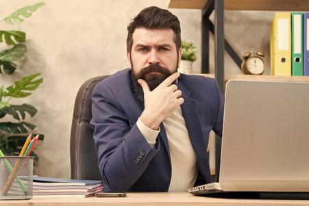 思考主要目标.留着胡子的老板坐在办公室里,手里拿着笔记本电脑照片