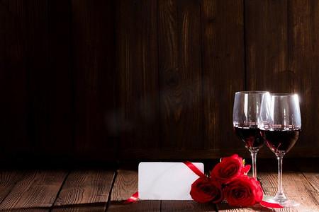 两杯红酒,红玫瑰和空白贺卡在深色木制背景浪漫约会*节.酒杯地板