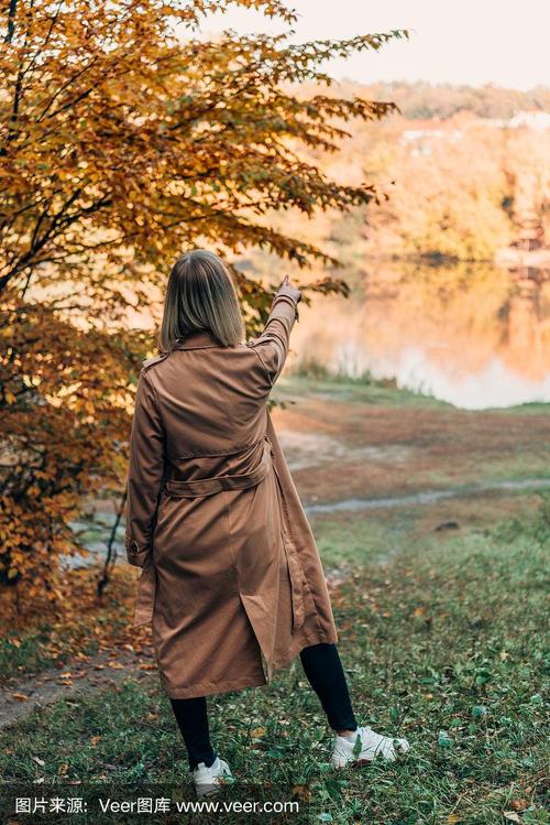 背影女子站在大衣和指向湖在秋天的森林
