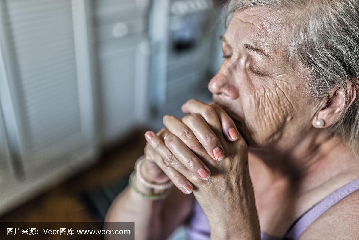 一位正在祈祷的老妇人.在家里祈祷的老年妇女